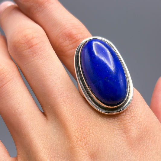 Hand wearing a ring with a blue stone on a gray background